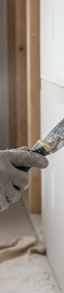 A close-up shot showing a hand using a utility knife to carefully cut out a section of bubbling drywall tape from a painted white wall.
