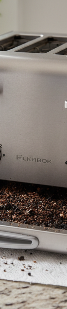 A modern stainless steel toaster with a slice of bread popping out, sitting on a clean kitchen counter next to a circuit breaker panel.