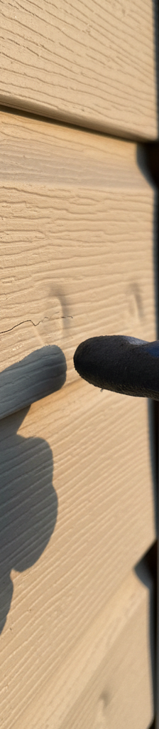 Close-up of vinyl siding with subtle hail damage, showing dents and a small crack highlighted by angled sunlight.