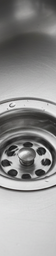 Kitchen sink with clear water slowly draining, indicating a partial clog in the pipes.