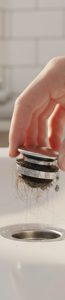 Hand removing a dirty pop-up stopper from a bathroom sink drain, illustrating a common source of bad odors