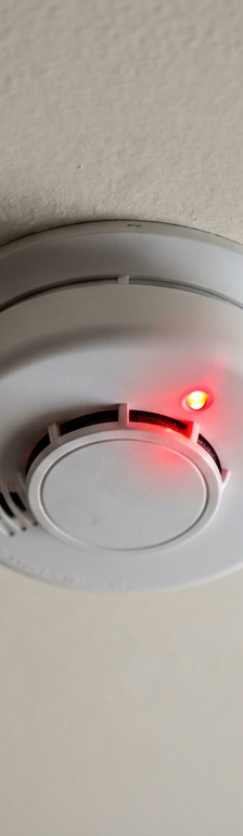 A ceiling-mounted smoke detector with a blinking red indicator light, signaling that it needs attention or is in a specific mode.