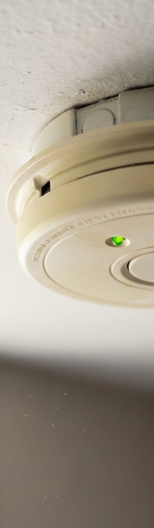 A hardwired smoke detector on a ceiling with a green power indicator light on.