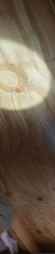 Homeowner in attic inspecting subtle water stain on roof decking with a flashlight.