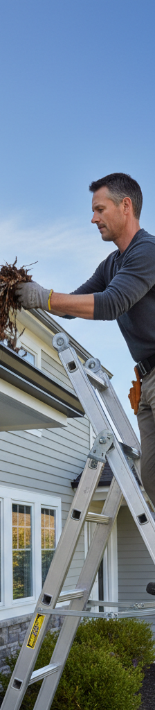 Homeowner cleaning gutters in spring as part of home maintenance checklist.