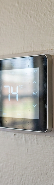 A digital thermostat on a wall showing an inaccurate temperature compared to a real thermometer next to it.