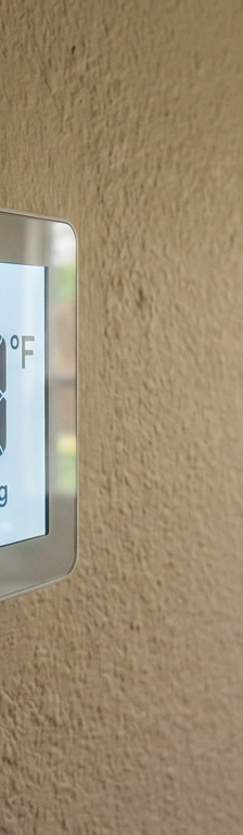 A digital thermostat on a wall showing that the current room temperature is higher than the set cooling temperature.