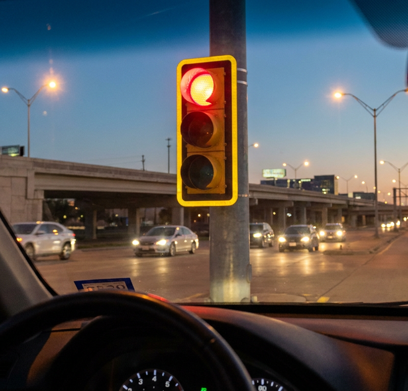 A close-up of a red traffic light with a reflective yellow border around it at dusk.