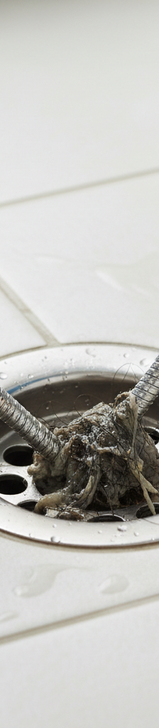 Person in gloves using a drain snake to clear a clogged shower drain, pulling out hair and soap scum.
