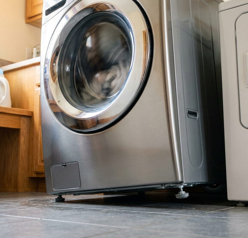 Washing machine vibrating violently on laundry room tile floor with off-balance drum during high-speed spin cycle