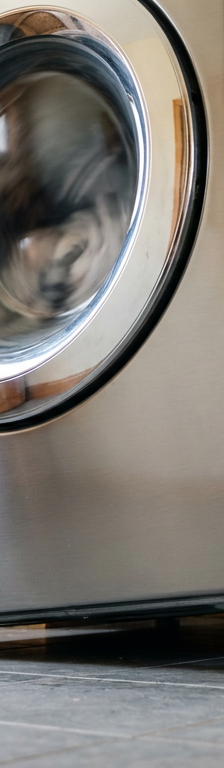 Washing machine vibrating violently on laundry room tile floor with off-balance drum during high-speed spin cycle