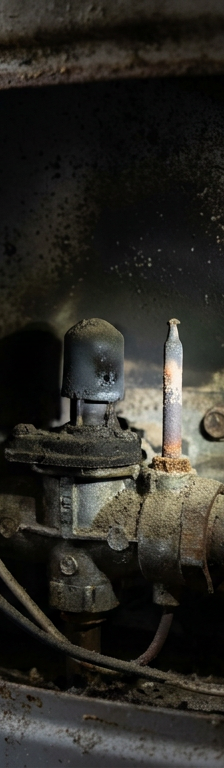 Close-up of an unlit pilot light and dirty thermocouple inside a gas water heater's burner chamber.