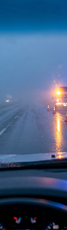 A driver's view of a construction truck with flashing blue and amber warning lights on the side of a highway.