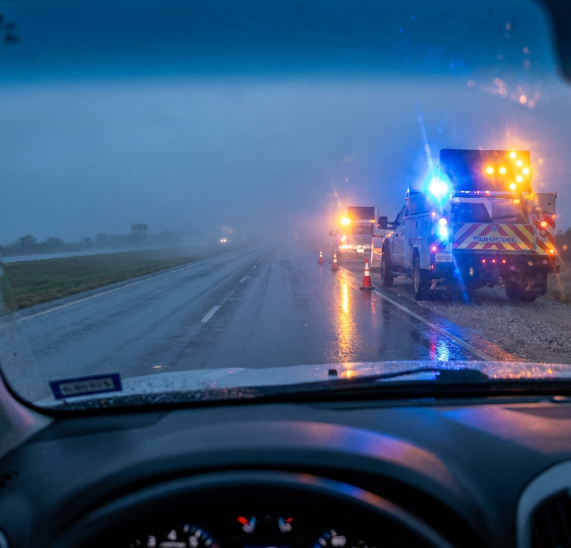 A driver's view of a construction truck with flashing blue and amber warning lights on the side of a highway.