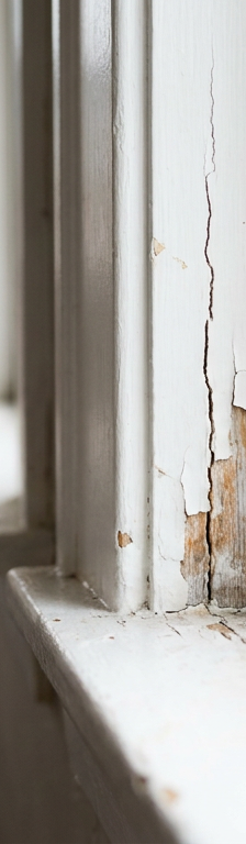 A close-up of a cracked white wood window frame showing where it needs to be repaired.